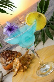 Blue cocktail on the tropical sea sunset background. Blue Lagoon margarita martini cocktail. Summer beach alcohol drink.  Iced blue cosmopolitan cocktail.