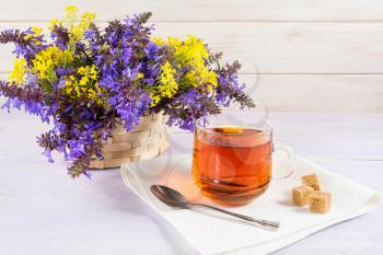 Cup of tea and wicker basket with purple and yellow flowers. Spring tea time concept. Breakfast tea cup served with flowers.