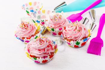 Cupcakes with pink whipped cream swirl and confectionery syringe. Birthday cupcake with pink whipped cream. Homemade decorated cupcakes. 