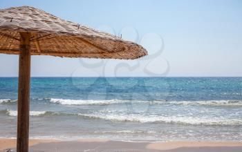 Tall umbrella standing in the sand. A wooden Bonita hut giving shade the shoreline. A bright sun shinning above the sea. Relaxing travel destination. Beach ideas