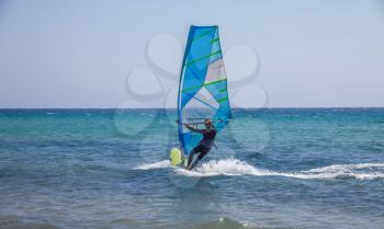 A man balancing the sailing board. Strong waves gliding below the water sport equipment. Windsurfing enthusiast in action. Promoting activity in the beach