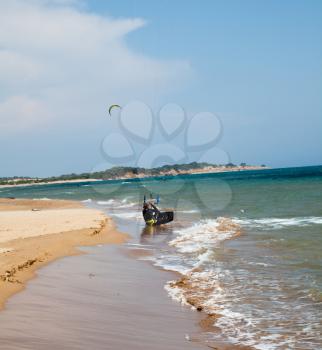 Sand beach on the sea. Man sitting on the sandy beach. Parachute sport in the background. Waves on the seashore. Action sport with parachute concept on the seaside.