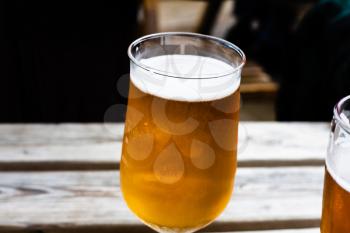 Glass of beer on the wooden table. Draft beer served at the bar. Glass of light beer on the wooden board. Alcoholic beverage with blurred background. Served alcoholic drinks in a glass.
