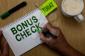 Conceptual hand writing showing Bonus Check. Business photo showcasing something in addition to what is expected or strictly due Man holding marker notebook reminder wooden table cup coffee