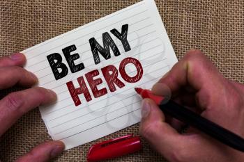 Writing note showing Be My Hero. Business photo showcasing Request by someone to get some efforts of heroic actions for him Man's hand hold white paper with symbolic letter jute sack background