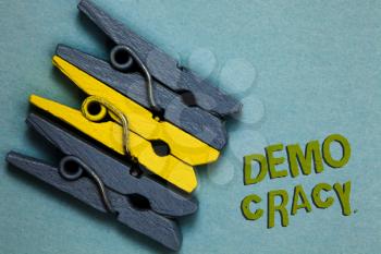 Conceptual hand writing showing Demo Cracy. Business photo text freedom of the people to express their feelings and beliefs Gray yellow vintage clothespins clear background Holding things