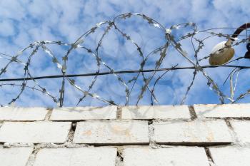 Old barbed wires and white brick wall against blue sky.