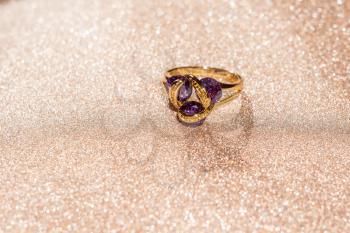 Fashion golden ring with purple amethyst on glittering background.