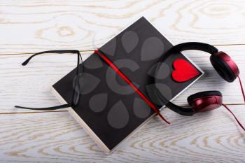 Headphones, notebook, pen, glasses and heart on a wooden background