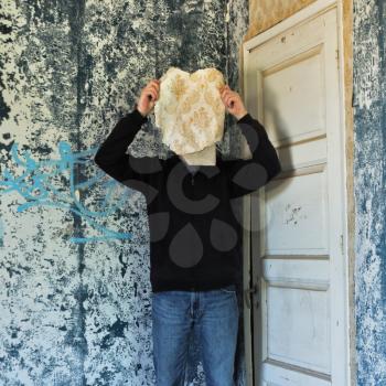 Figure obscured by torn wallpaper shred in decaying abandoned house interior.