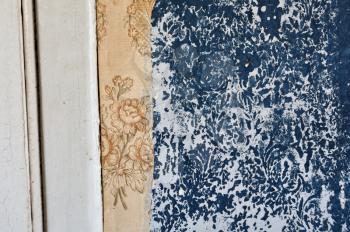 Torn vintage wallpaper and floral pattern imprinted on peeling paint wall.