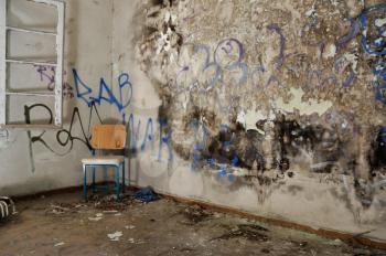 Chair in decayed room interior. Peeling moldy wall and smudged paint.