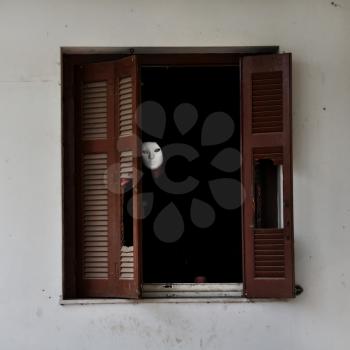 Man with white mask by the broken window shutter of an abandoned house.