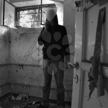 Hooded man obscured by piece of broken glass in decayed dirty room.