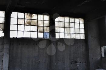 Broken windows and concrete wall in abandoned factory interior.