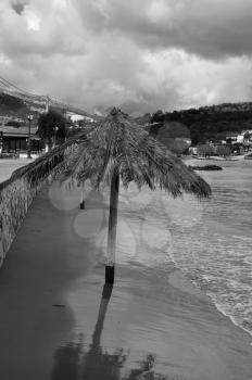 Sandy beach in the wintertime and parasol with palm tree leaves. Black and white.