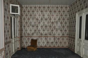Vintage chair and wall with retro wallpaper pattern in empty living room of an abandoned house.