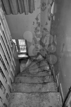 Crooked wooden staircase and peeling paint wall in abandoned house. Black and white.