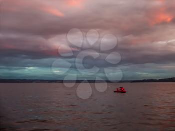 A jetski is anchored at Three Tree Point, Washington as the sun sets.  Pink and purple billowing clouds  blanket the Puget Soiund.