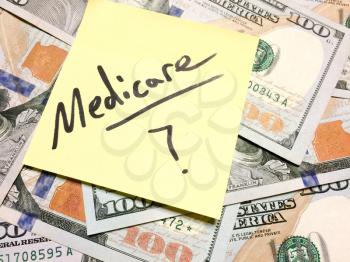 American cash money and yellow sticky note with text Medicare with question mark in black color aerial view
