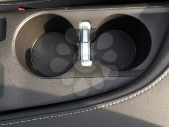 Cup bottle holder in car made of black plastic near leather stitched seat