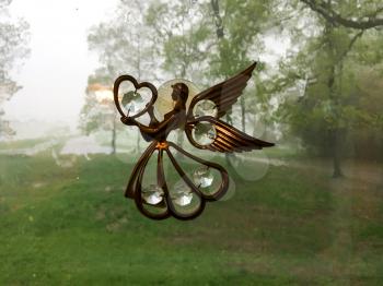 Angel ornament on window on rainy day in gold brass