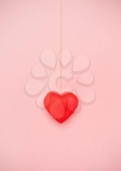 Heart hanging to a string of twine on pink background. Love concept hanging by a thread.