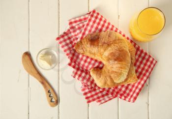 Fresh homemade croissant on checkered tableclothe with butter and a glass of orange juice.  Top view.
