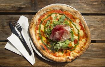 Top view of a ham and cheese pizza with rucola and pesto on a rustic wooden table
