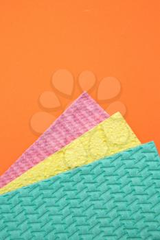 Top view of three different colours of cleaning sponges  on an orange background