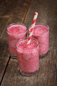 Three strawberry smoothies with straw on a wooden background