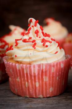 White cupcake with vanilla icing and red candies in a pink polka dots paper.