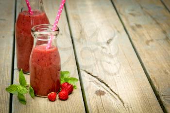 Strawberry smoothie freshly made in a jar with a lined straw on rustic wood