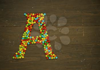 Letter A from alphabet made with star shape candy on a wooden background