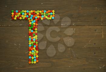 Letter T from alphabet made with star shape candy on a wooden background