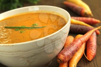 Close up of a vegetables soup with fresh carrots on a wooden table