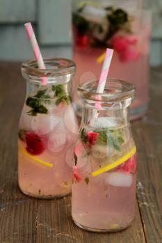 Bottles of pink lemonade with raspberry and mint standing on a wood background